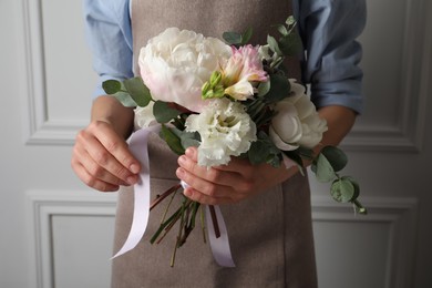 Florist creating beautiful bouquet at white wall, closeup