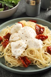Delicious spaghetti with burrata cheese and sun dried tomatoes on grey table, closeup