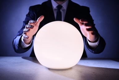 Businessman using glowing crystal ball to predict future at table, closeup. Fortune telling