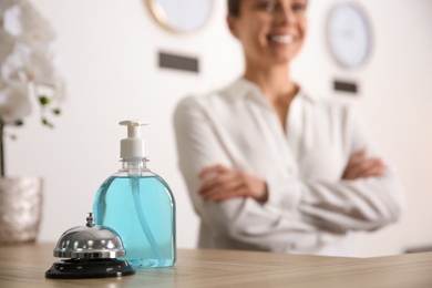 Receptionist at countertop in hotel, focus on dispenser bottle with antiseptic gel and service bell