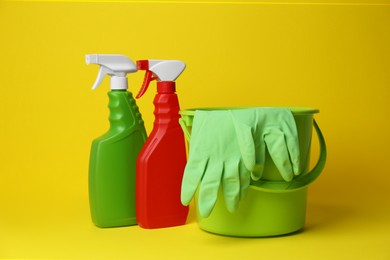Photo of Green bucket, gloves and detergents on yellow background. Cleaning supplies