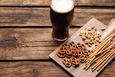 Glass of beer served with delicious pretzel crackers and other snacks on wooden table. Space for text
