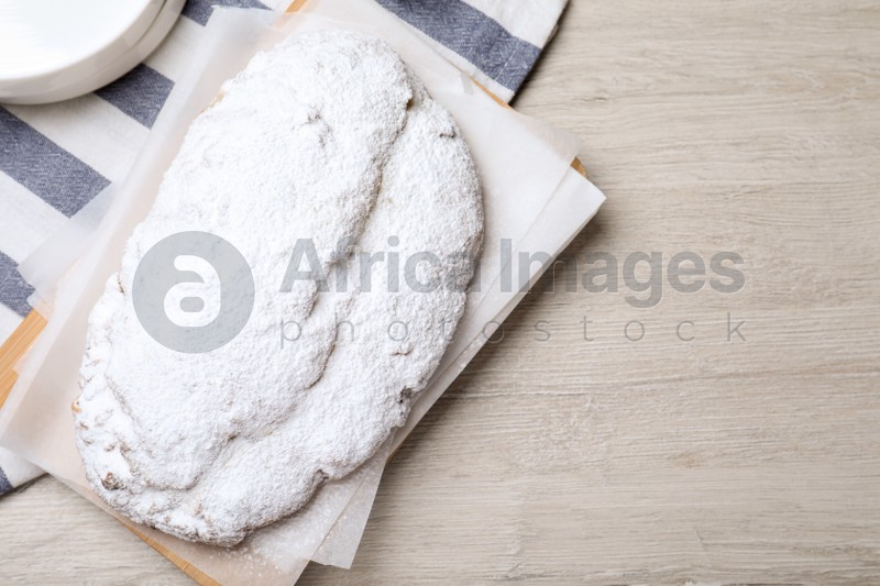 Delicious Stollen sprinkled with powdered sugar on wooden table, top view. Space for text