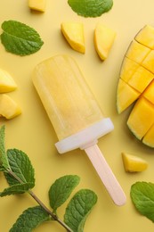 Photo of Tasty mango ice pop on light yellow background, flat lay. Fruit popsicle