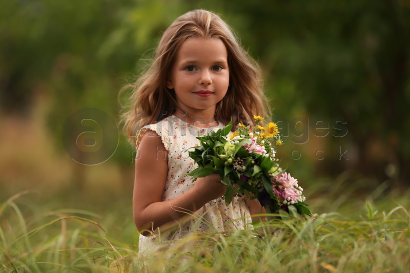Cute little girl holding wreath made of beautiful flowers in field