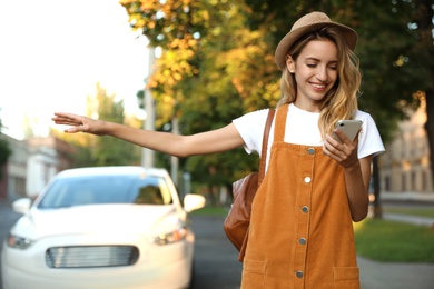 Young woman with smartphone catching taxi on city street