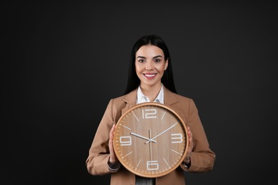 Businesswoman holding clock on black background. Time management