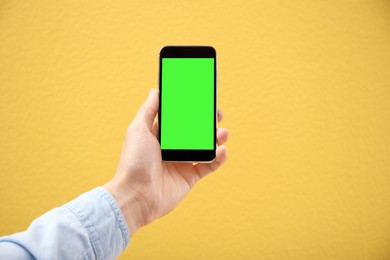 Image of Man holding smartphone with green screen on yellow background, closeup. Gadget display with chroma key. Mockup for design
