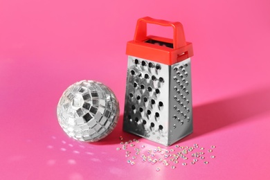 Grater and silver disco party ball on pink background