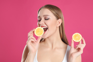 Young woman with cut lemon on pink background. Vitamin rich food