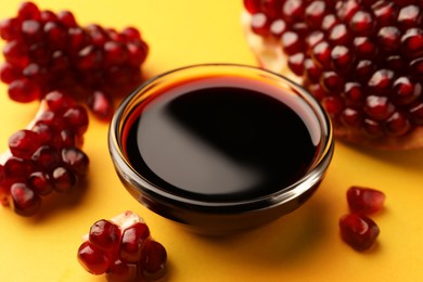 Photo of Glass bowl of tasty pomegranate sauce and fresh ripe fruit on yellow background, closeup