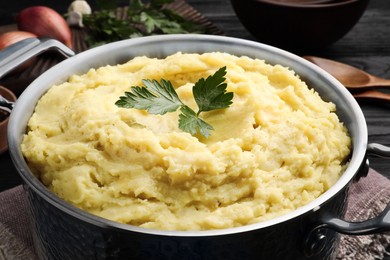 Photo of Pot of tasty mashed potatoes with parsley on black wooden table, closeup