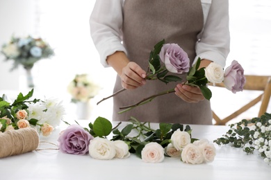 Florist making beautiful wedding bouquet at white table, closeup