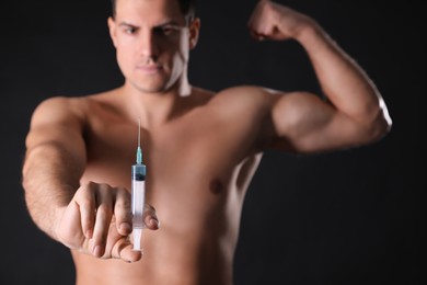 Athletic man with syringe against black background, focus on hand. Doping concept