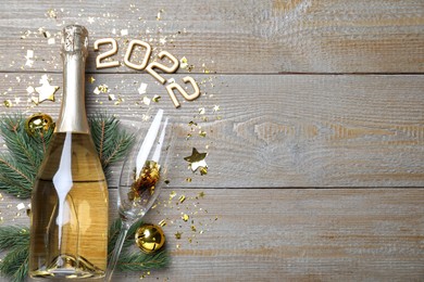 Happy New Year 2022! Flat lay composition with bottle of sparkling wine on wooden table, space for text