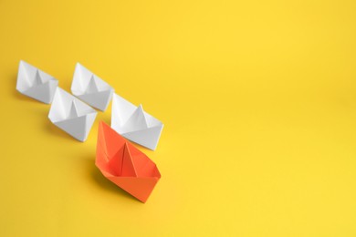 Photo of Group of paper boats following orange one on yellow background, space for text. Leadership concept