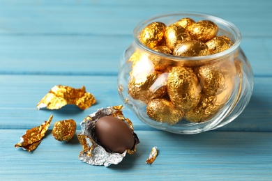 Chocolate eggs wrapped in golden foil on light blue wooden table