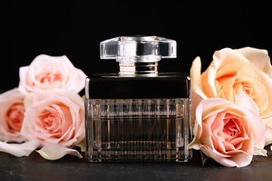 Bottle of perfume and beautiful roses on black table