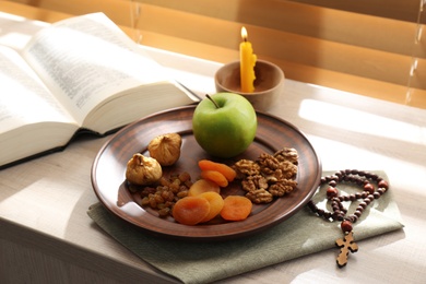 Dried fruits, apple, prayer beads, Bible and candle on window sill indoors. Great Lent season
