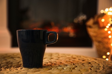 Dark blue cup with hot drink against fireplace, space for text