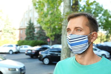 Man wearing handmade cloth mask outdoors, space for text. Personal protective equipment during COVID-19 pandemic