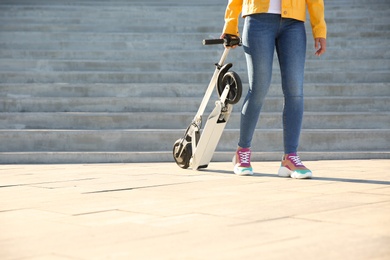 Woman carrying folded electric kick scooter outdoors. Space for text