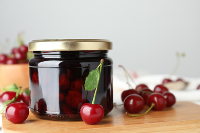 Jar of pickled cherries and fresh fruits on wooden board, closeup