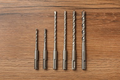 Different drill bits on wooden table, flat lay