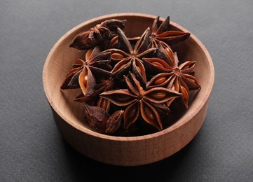Aromatic anise stars in wooden bowl on grey background