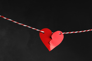 Broken red paper heart on rope against black background. Relationship problems concept
