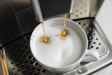 Modern coffee machine making cappuccino into cup, closeup