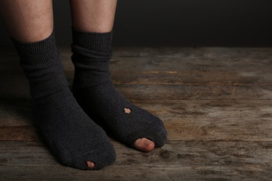 Poor person in shabby socks on wooden floor, closeup