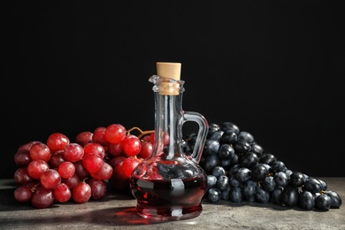 Glass jug with wine vinegar and fresh grapes on gray table against black background