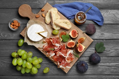 Photo of Board with delicious figs, proscuitto, cheese and grapes on grey wooden table, flat lay