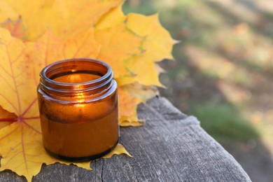 Burning candle and beautiful dry leaves on wooden surface outdoors, closeup with space for text. Autumn atmosphere