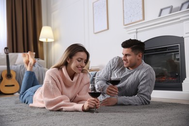 Happy couple with glasses of wine resting near fireplace at home