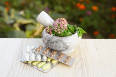 Mortar with fresh herbs and pills on wooden table outdoors