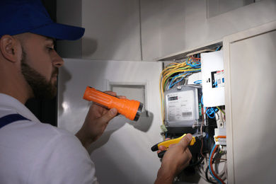 Electrician with flashlight fixing electric panel indoors