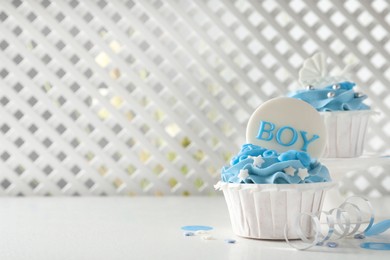 Photo of Delicious cupcakes with light blue cream and toppers on white table, space for text. Baby shower party