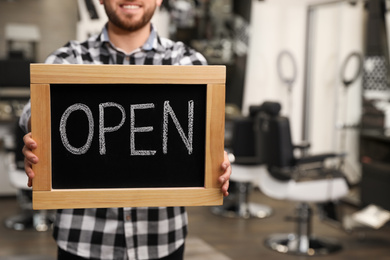 Photo of Young business owner holding OPEN sign in his barber shop, closeup