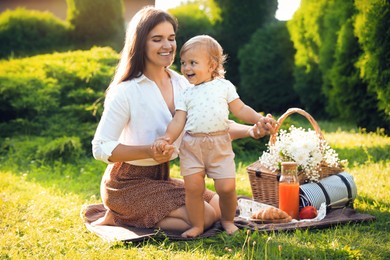 Photo of Mother with her baby daughter having picnic in garden on sunny day