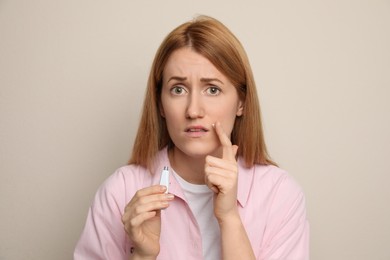 Upset woman with herpes applying cream on lips against beige background
