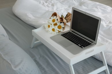 White tray table with laptop and bouquet of beautiful daisies on bed