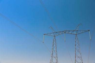 High voltage tower with electricity transmission power lines against blue sky, low angle view