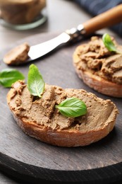 Slices of bread with delicious pate and basil on wooden board, closeup