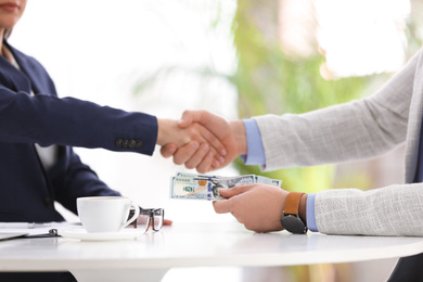 Man shaking hands with woman and offering bribe at table in office