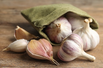 Fresh unpeeled garlic bulbs and sack on wooden table, closeup. Organic product