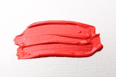 Smear of red paint on white background, top view