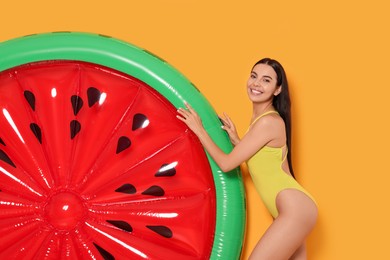 Photo of Young woman in stylish swimsuit near inflatable mattress against orange background