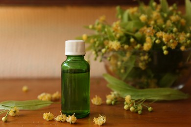 Bottle of essential oil and linden blossoms on wooden table. Space for text